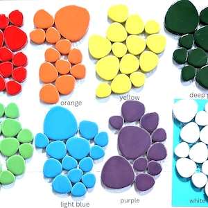 May include: A collection of eight color-coded groups of smooth, pebble-shaped ceramic tiles arranged in clusters. The colors include red, orange, yellow, deep green, lime, light blue, purple, and white, with each group labeled by its color name.