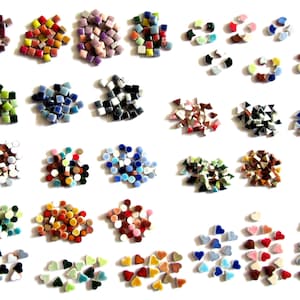 May include: A collection of small ceramic mosaic tiles in various shapes including squares, circles, triangles, and hearts. The tiles are arranged in multiple color-coded groups featuring shades of red, blue, green, yellow, pink, and black.