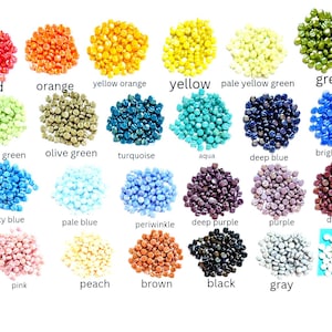 May include: A collection of small, round wax seal beads arranged in twenty-four distinct color piles. Each pile is labeled with its corresponding color name, including red, orange, yellow, green, blue, purple, pink, brown, black, gray, and white.