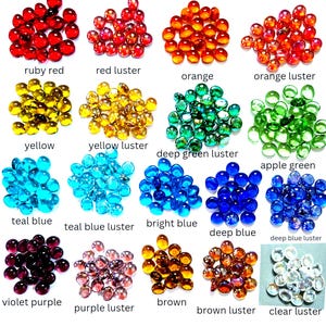 May include: A collection of small, round, flat-bottomed glass gems arranged in sixteen distinct colour groups. The colours include ruby red, red lustre, orange, orange lustre, yellow, yellow lustre, deep green lustre, apple green, teal blue, teal blue lustre, bright blue, deep blue, deep blue lustre, violet purple, purple lustre, brown, brown lustre, and clear lustre.