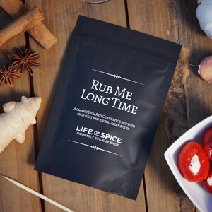 May include: A black pouch with white text that reads "Rub Me Long Time" and "A classic Thai Red Curry Spice Rub with mild heat and exotic Asian spices." Below the text is "Life of Spice Gourmet Spice Blends."