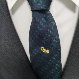 May include: A dark blue tie with a green leaf pattern and a gold monogram that reads "GJM".