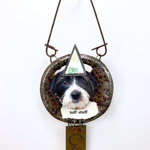 May include: A rusty metal ornament with a black and white dog face, a green owl, and the text "tuff stuff". The ornament is hanging from a wire loop and has a gold metal tag with the letter "C" on it.