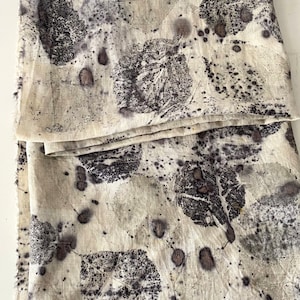 May include: A piece of white linen fabric with a dark grey leaf pattern. The fabric has a natural, organic look and feel.