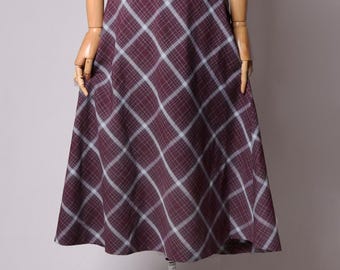 May include: A burgundy plaid skirt displayed on a mannequin. The skirt features a classic plaid pattern in burgundy and light blue. The skirt is knee-length and has a flared silhouette.
