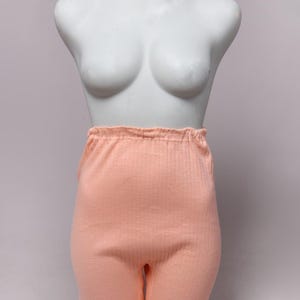 May include: Peach-colored, ribbed knit shorts displayed on a white mannequin. The shorts have an elastic waistband and a fitted leg. The fabric appears soft and comfortable, suitable for sleepwear or loungewear.