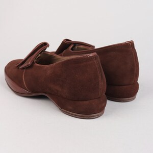 May include: A pair of brown suede loafers with a tassel detail. The loafers have a low wedge heel.