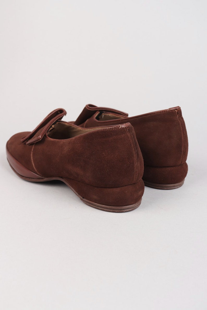 May include: A pair of brown suede loafers with a tassel detail. The loafers have a low wedge heel.