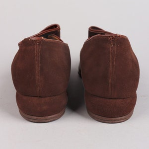 May include: A pair of brown suede shoes with a pointed toe and a low heel. The shoes have a strap across the top of the foot and a buckle closure.