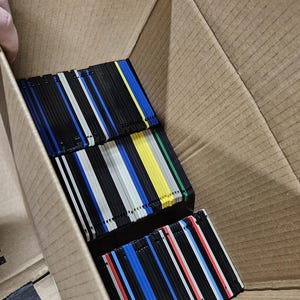 Op de afbeelding: Een kartonnen doos gevuld met meerdere stapels vierkante 3,5-inch diskettes. De diskettes zijn in rijen gerangschikt en hebben verschillende kleuren, waaronder zwarte, blauwe, gele, grijze en rode plastic behuizingen met metalen schuifklepjes.