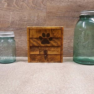 May include: A wooden box with a paw print design, two clear glass jars with lids, one large and one small.