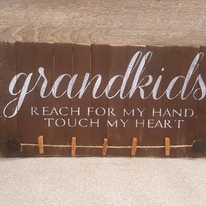 May include: A brown wooden sign with the text "grandkids reach for my hand, touch my heart" in white lettering. The sign has a rustic look and is decorated with clothespins.
