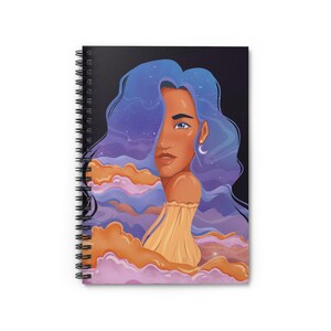 Op de afbeelding: Spiraalgebonden notitieboek met een illustratie van een vrouw met blauw haar en een sterrenhemelontwerp. Het kunstwerk bevat een gele jurk en een maanvormige oorbel. De achtergrond is een donkere nachthemel met sterren en wolken.