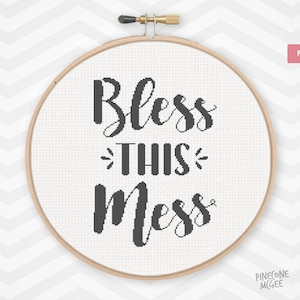 May include: A white embroidery hoop with the text "Bless this mess" in black lettering. The hoop is on a white and gray chevron background.