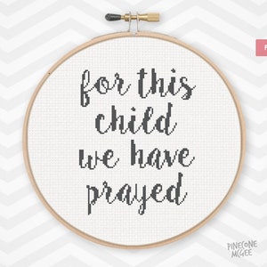 Può includere: Un cerchio da ricamo bianco con il testo "for this child we have prayed" in corsivo nero. Il cerchio è su uno sfondo bianco e grigio a chevron.