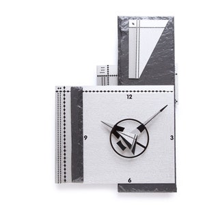 May include: Abstract wall clock with a geometric design. The clock features a white face with black hands and a black circular design. The clock is accented with black and gray rectangular shapes and dotted lines. The numbers 3, 6, 9, and 12 are visible.