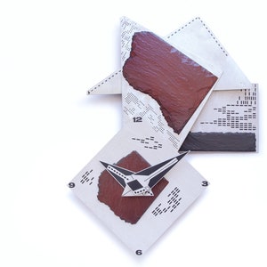 May include: Abstract wall clock with a geometric design. The clock features a white background with a diamond-shaped face, a red-brown center, and black and silver hands. Numbers 3, 6, 9, and 12 are visible.