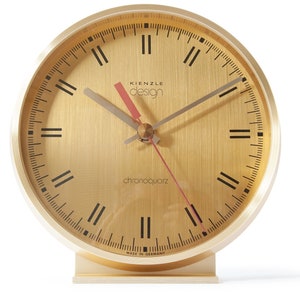 Könnte beinhalten: Eine goldfarbene Analoguhr mit römischen Ziffern und einem gebürsteten Metallzifferblatt. Das Zifferblatt der Uhr zeigt "Kienzle Design chronoquartz Made in Germany".