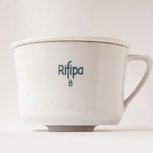 Könnte beinhalten: Weiße Keramiktasse mit einem grünen Logo, auf dem "Riffipa B" steht.