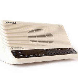 May include: Cream-colored vintage Siemens radio with a speaker, control panel, and the text "Siemens" and "RG 317". The radio has a ridged design and a black control panel with buttons and a display.