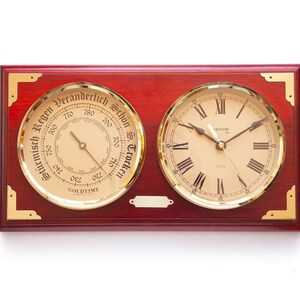 May include: A mahogany wood framed wall clock and barometer with gold accents. The clock face has Roman numerals and the barometer has a dial with German text indicating "Stürmisch Regen" (stormy rain) to "Schön Trocken" (fair dry).