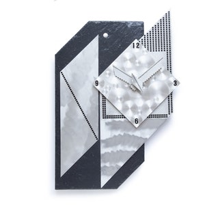 May include: Abstract wall clock with a geometric design. The clock features a black and silver color scheme with a textured surface. The clock hands are silver, and the numbers 3, 6, 9, and 12 are visible.