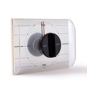 Peut inclure: Un minuteur en plastique blanc avec un bouton noir et un cadran transparent. Le cadran est marqué en noir pour les minutes et les mots "SIGNAL" et "KIEN."