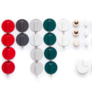 Può includere: Una collezione di manopole rotonde in vari colori, tra cui rosso, nero, bianco, verde e oro. Le manopole hanno una piccola linea rialzata al centro e sono disposte in uno schema che compone la parola "FTP".