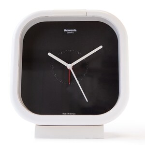 May include: White square alarm clock with a black face and white hands. The clock has a silver trim and the words "Rowenta Quartz" printed on the face.