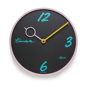 May include: A black and pink round wall clock with a yellow hand and turquoise numbers. The clock face says "timestyle" and "Hermle Made in Germany".