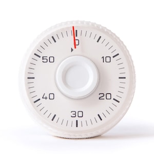 Puede incluir: Temporizador redondo blanco con una aguja roja apuntando al número 0. El temporizador tiene marcas negras para los números 10, 20, 30, 40, 50 y 60.