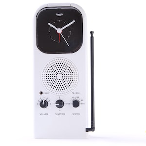 May include: White retro-style clock radio with a black clock face and a black antenna. The clock face has white hands and red second hand. The radio has volume, function, and tuning knobs. The speaker is a circular design.
