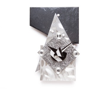 May include: A modern clock with a silver face and black numbers. The clock is made of metal and has a geometric design. The clock is mounted on a white wall.