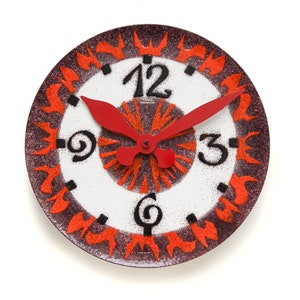 May include: A round, white clock face with black numbers and hands. The clock face is surrounded by a brown and orange ring with a flame design. The clock hands are red.