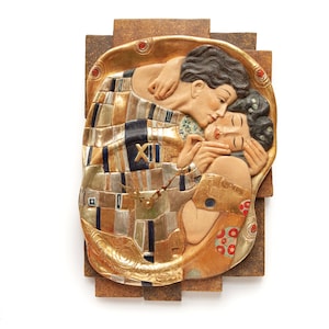 Puede incluir: Un reloj de pared rectangular con una escultura en relieve de una pareja abrazándose, inspirada en "El Beso" de Gustav Klimt. El reloj tiene una combinación de colores dorados, marrones y azules, con números romanos y manecillas. El reloj está montado sobre un fondo marrón.