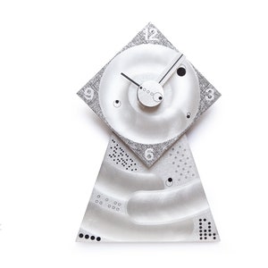 May include: A silver clock with a unique design. The clock face is a square with rounded corners and the numbers are printed in a circular pattern. The clock hands are silver and the clock is mounted on a triangular base.