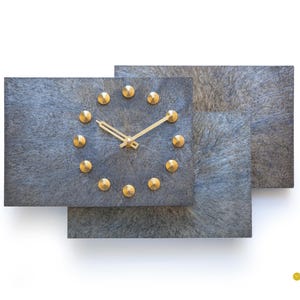 May include: A gray and blue geometric wall clock with gold accents. The clock face has a circle of gold studs around the edge and gold hands.