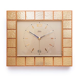 May include: A rectangular vintage clock with a gold-toned frame and a light beige face. The frame is divided into squares with a textured pattern. The clock face features gold-colored markers and hands, with the text "Dial Electronic".