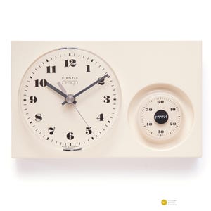 Puede incluir: Reloj Kienzle design de color crema con una esfera redonda y un dial de temporizador más pequeño. La esfera del reloj tiene números y manecillas negras. El dial del temporizador también es de color crema con marcas negras. El reloj es rectangular.