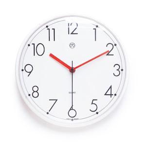 May include: A round wall clock with a white face, black Arabic numerals, and a thin black circular border. The clock features bright red hour and minute hands, a thin black second hand, and a small logo above the center. The word QUARTZ is printed.