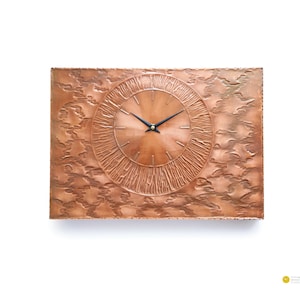 May include: A rectangular copper-colored wall clock with a textured surface. The clock face is circular with a sunburst design and black hands. The clock's hands point to 10:10. The clock is a vintage item.