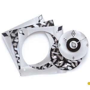 May include: A modern wall clock with a unique design. The clock features a circular face with black hands and a black center. The clock is accompanied by three square frames with a circular cutout and a black and white brushstroke pattern.