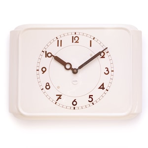 May include: A white square clock with black hands and brown numbers. The clock face has a white background with a black circle in the center. The clock is set to 10:10.