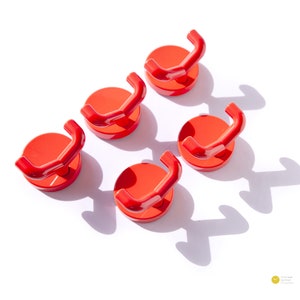 Puede incluir: Conjunto de cinco ganchos de plástico rojo con base redonda. Los ganchos están diseñados para montarse en una pared u otra superficie.