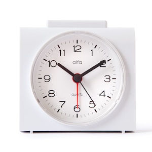 May include: White analog alarm clock with black hands and black numbers on a white face. The clock face says "alfa quartz".
