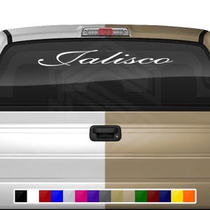 以下が含まれることがあります： ピックアップトラックのリアウィンドウに、「ハリスコ」という単語が筆記体で書かれた白いステッカー。トラックは白とベージュです。