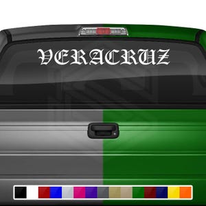 May include: A white truck with a green tailgate. The rear window has a white vinyl decal that reads "VERACRUZ" in a gothic font.