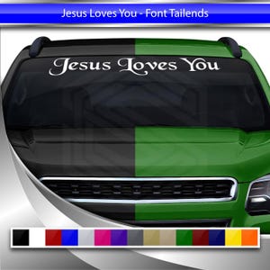 May include: A white decal with the text "Jesus Loves You" on a black and green car windshield.