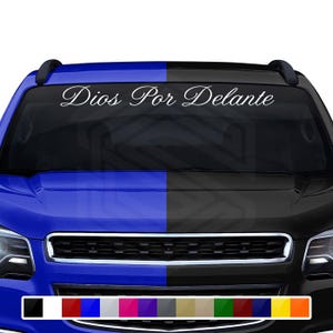 May include: A white vinyl decal with the text "Dios Por Delante" in a script font, designed to be applied to a vehicle's windshield. The image shows a blue and black car with a color palette of available decal colors.