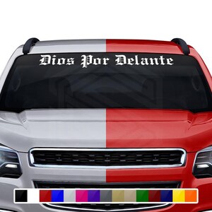 May include: White vinyl car windshield decal with the text "Dios Por Delante" in a gothic font. The decal is displayed on a silver and red car. A color palette of available colors is shown at the bottom.